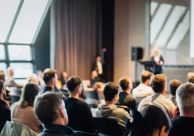 Delegates seated in a conference hall watching two speakers present on stage