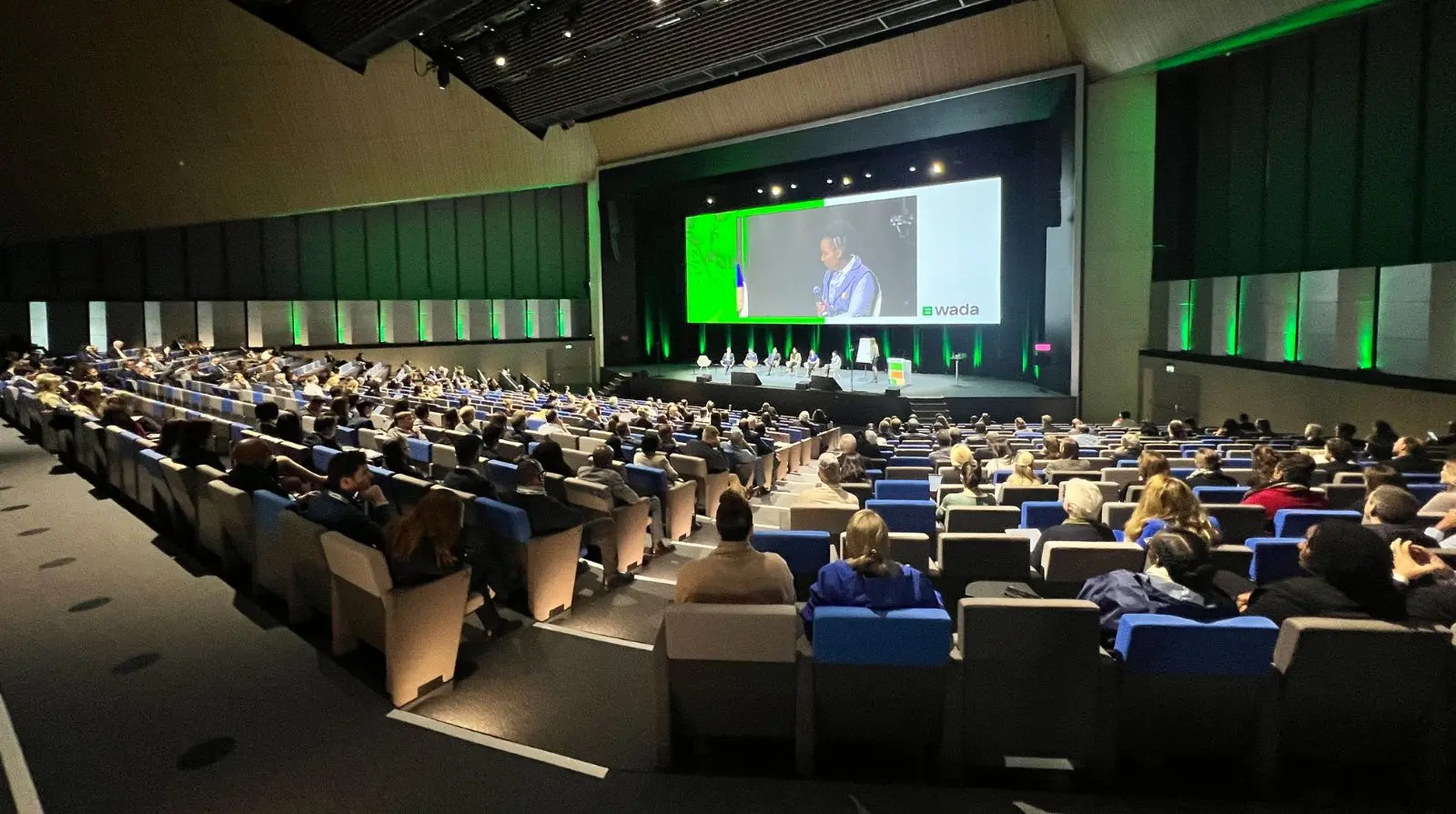 Conference delegates attending a keynote session during the WADA Annual Symposium in a large auditorium.