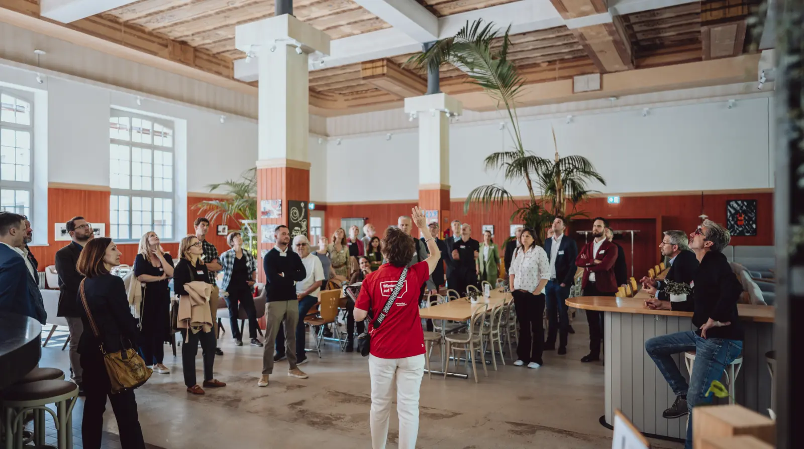 Delegates networking at a standing reception inside a bright, high-ceilinged industrial venue with white walls and palm trees in Winterthur.