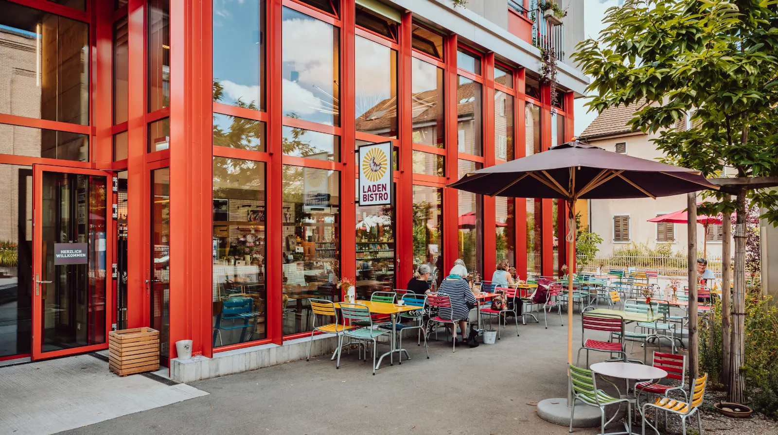 Terrace seating outside a modern café or restaurant with red-framed floor-to-ceiling windows and outdoor tables in Winterthur.