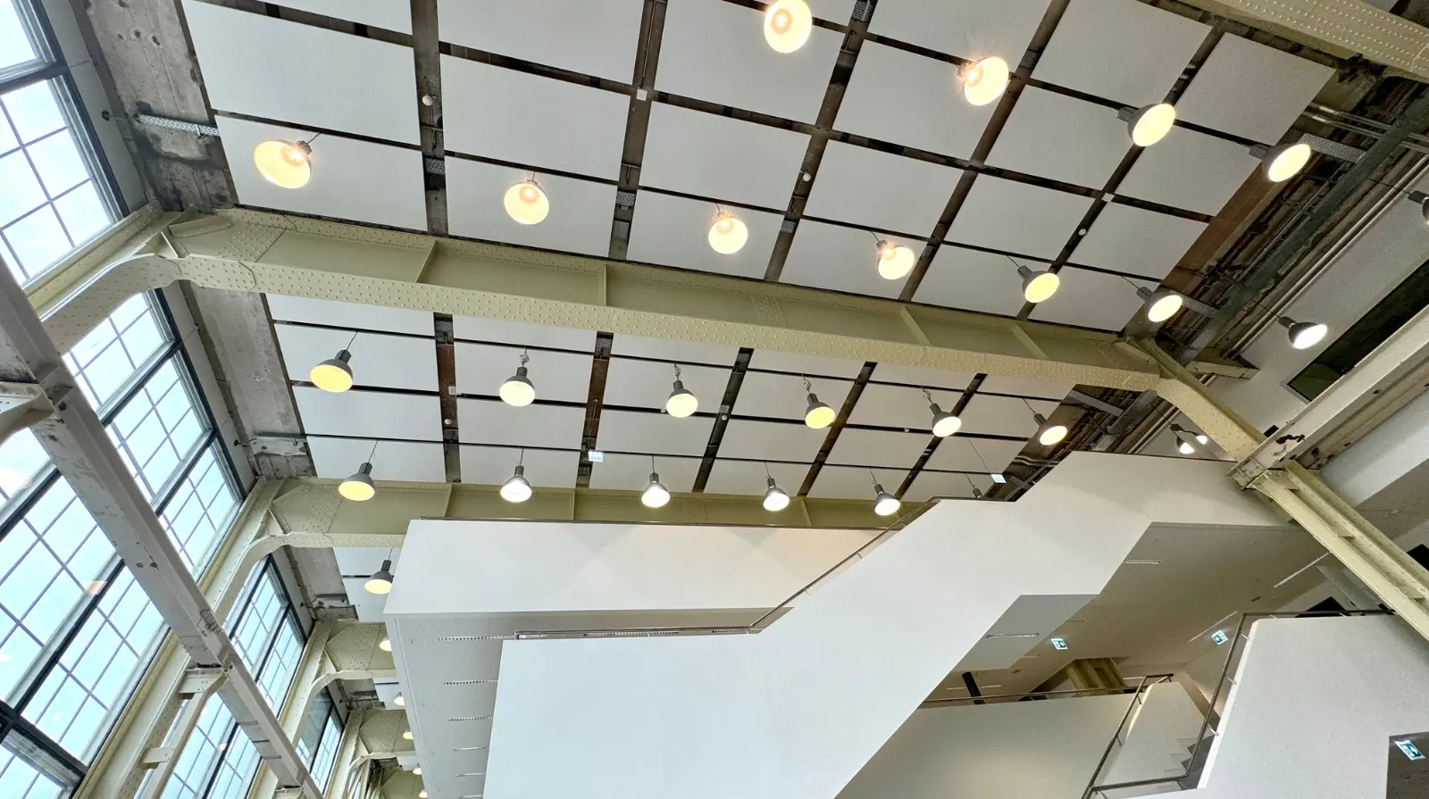 Modern interior of a large glass-roofed atrium with white structural beams, natural light and open gallery-style walkways.