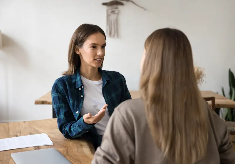 Professional discussing accommodation arrangements with a colleague during a meeting at a desk.