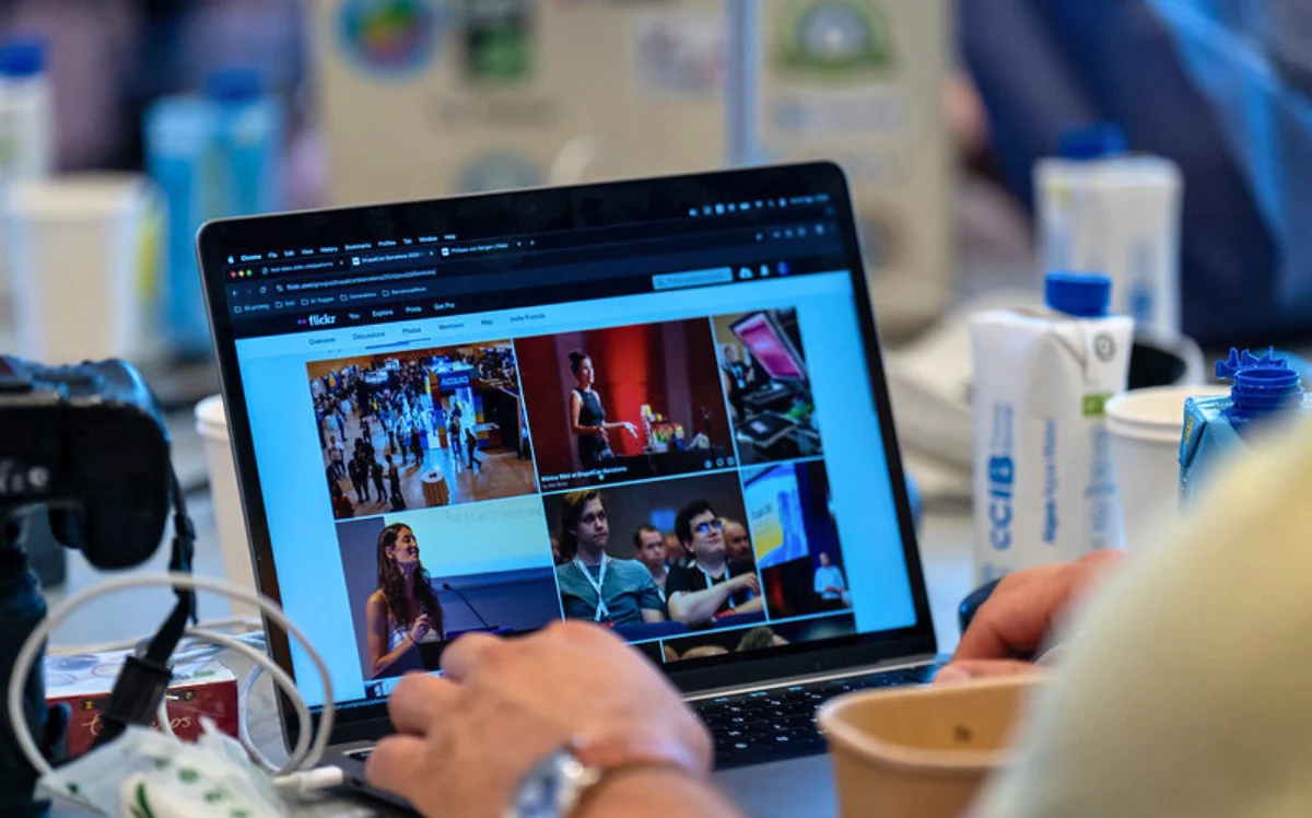 Close-up of hands on a laptop keyboard at a congress, screen showing a Flickr grid of event photographs