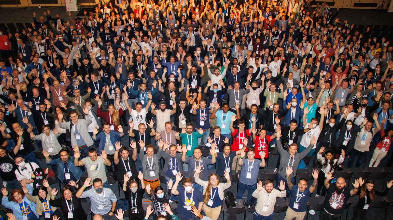 Hundreds of DrupalCon Europe delegates seated in an auditorium, raising their hands together for a group photo.