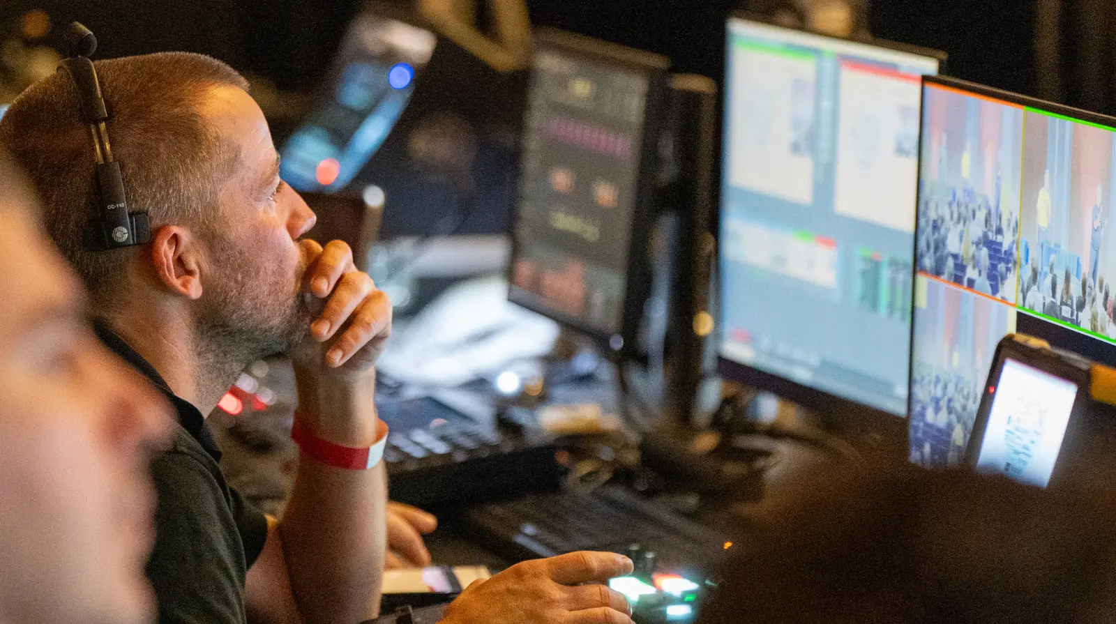 Audio-visual technician monitors multiple screens from the production desk, managing the live stream and stage feed for a DrupalCon Europe session.