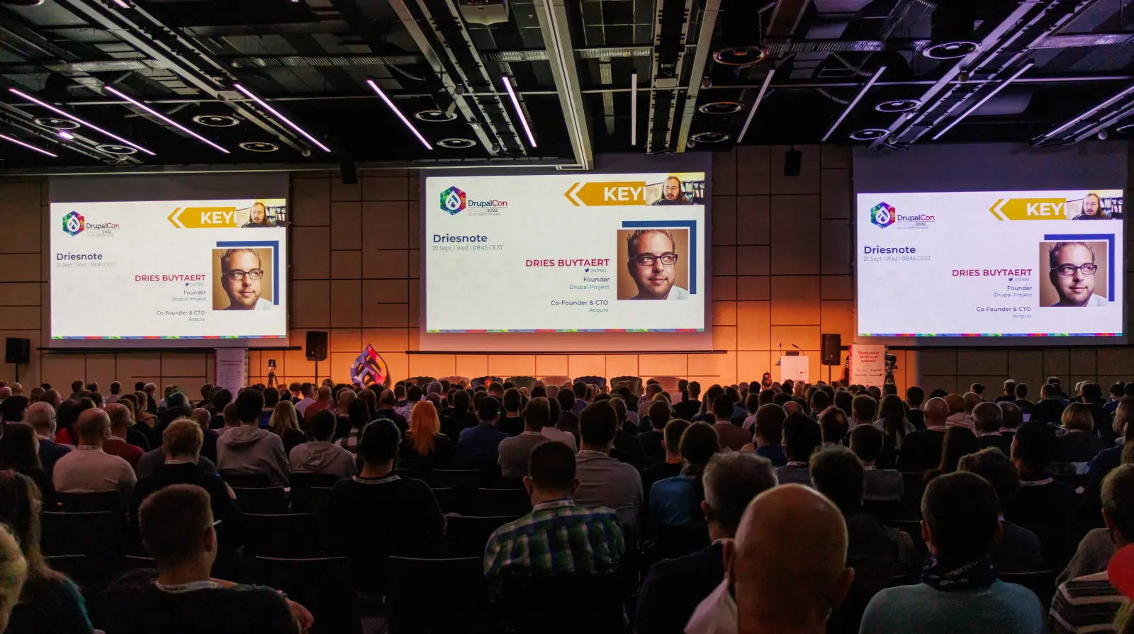 Audience watches the Driesnote keynote by Drupal founder Dries Buytaert across three large screens at DrupalCon Europe 2022.