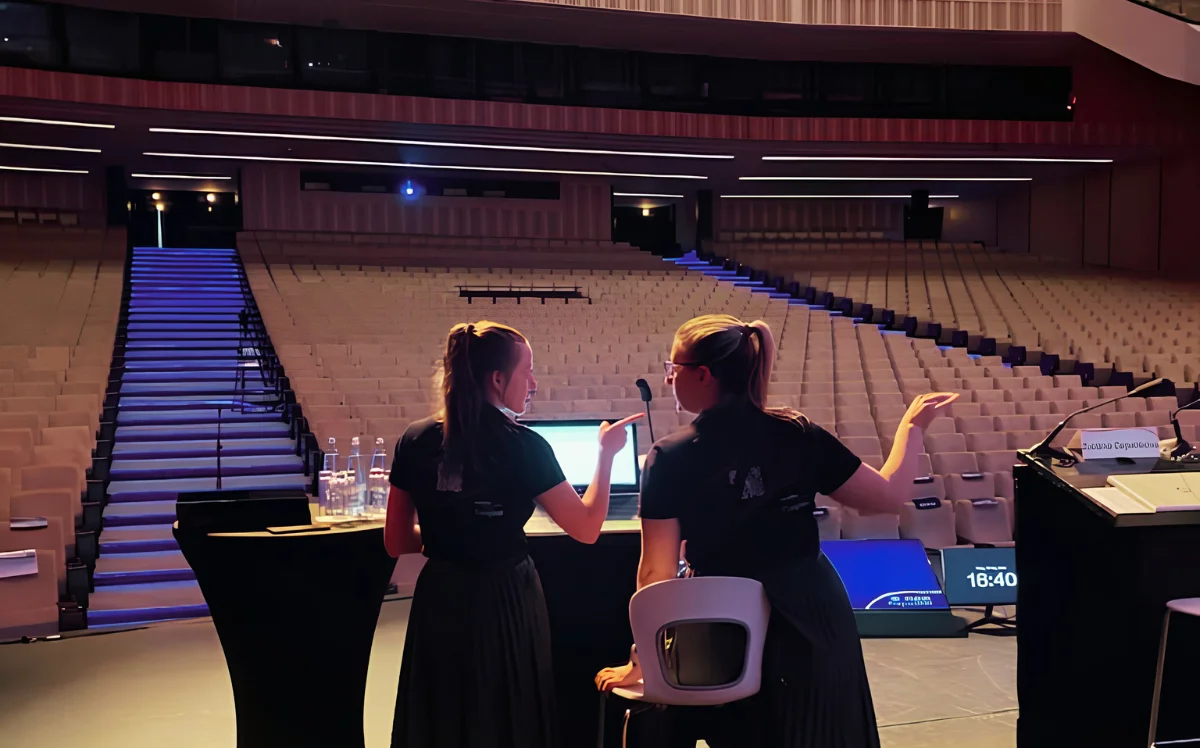 Two Kuoni Tumlare colleagues stand on stage in an empty auditorium, discussing plans for an upcoming congress.