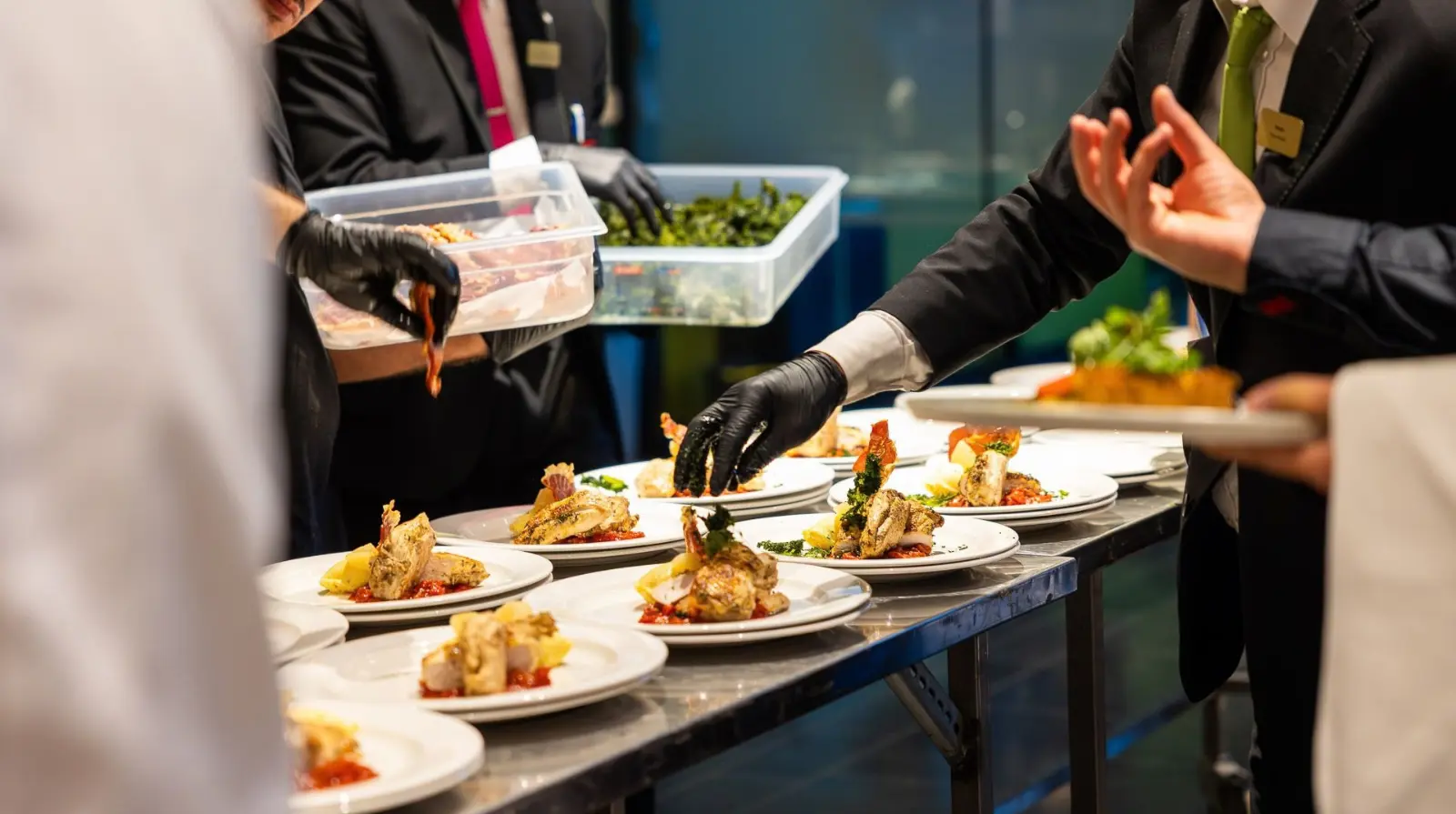 Event staff plating hot meals on a service line before a congress break.
