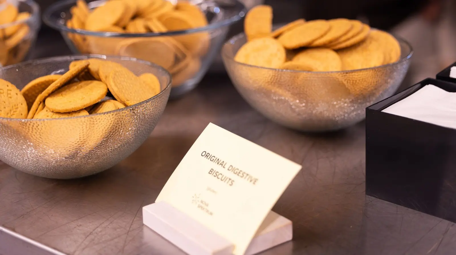 Glass bowls of biscuits on a counter beside a printed Original digestive biscuits label.