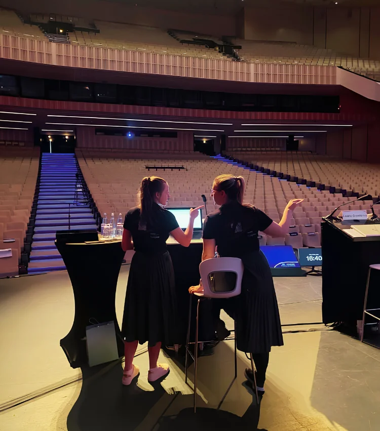 Two Kuoni Tumlare colleagues stand on stage in an empty auditorium, discussing plans for an upcoming congress.