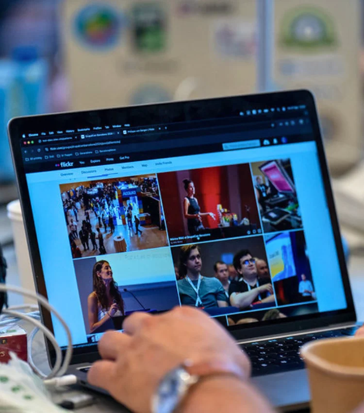 Close-up of hands on a laptop keyboard at a congress, screen showing a Flickr grid of event photographs