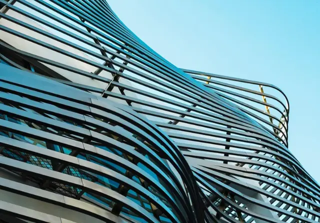 The sweeping curved glass facade of a contemporary congress centre against a blue sky