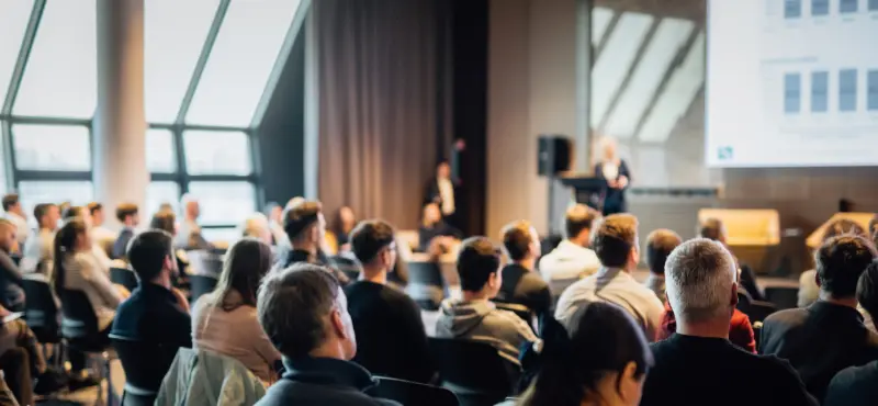 Delegates seated in a conference hall watching two speakers present on stage