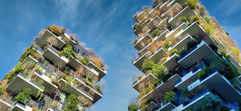 Two high-rise residential towers covered in lush greenery and vertical gardens against a blue sky